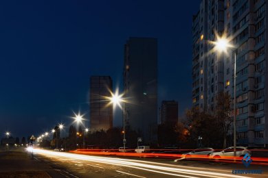 Опори вуличного освітлення в місті, на фоні будинків та дороги в сутінках